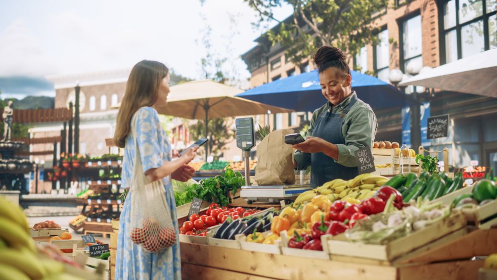 Female Customer Buying Sustainable Organic Vegetables From a Joyful Black Female Farmer on a Sunny Summer Day.