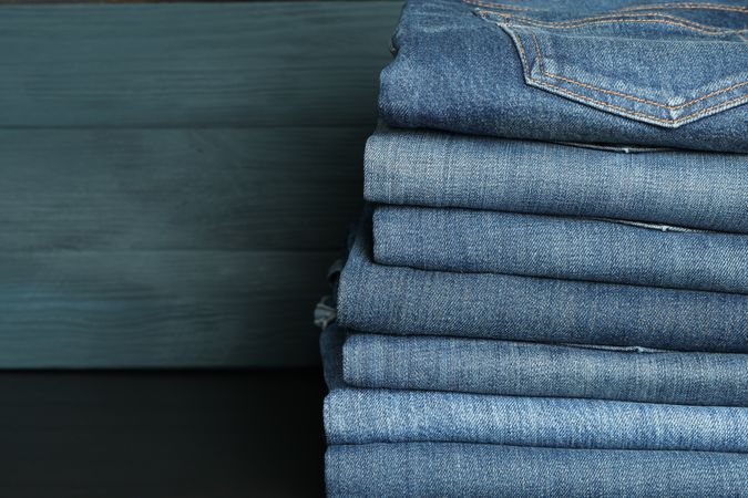 Stack of jeans pants on table, space for text