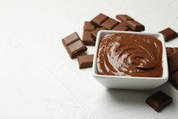 Bowl with chocolate and chocolate pieces on neutral background