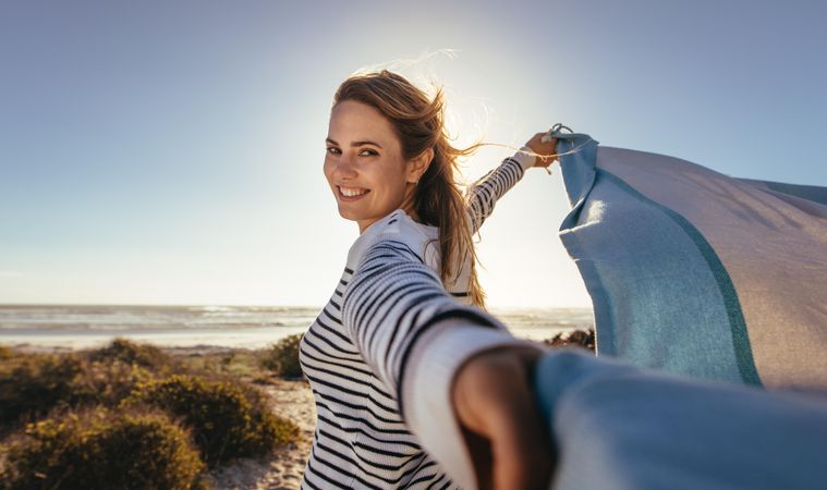 Portrait of a smiling woman holding a drape against the sea breeze