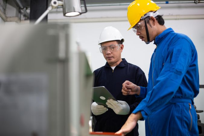 Asian man in blue jumpsuits and hard hats working in industrial factiory