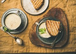 Top view of two cups of celery soup with toast, and spoon, on wooden board