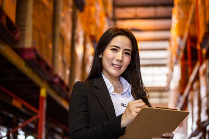 Business woman or manager smiling and writing on clipboard at warehouse factory