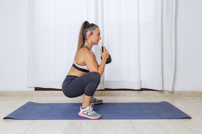 Young woman couching and doing legs workout using kettlebell