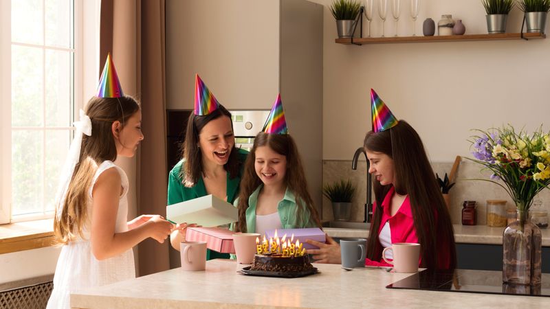 Family gathered around as girl opens gifts, smiling and excited.