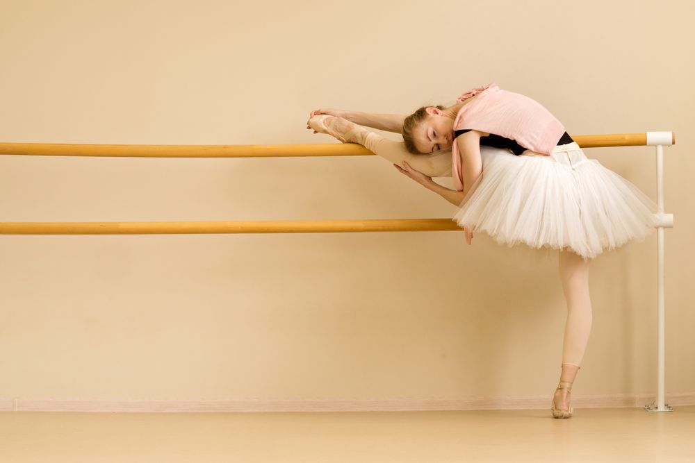 Ballet dancer stretches by placing her leg on barre