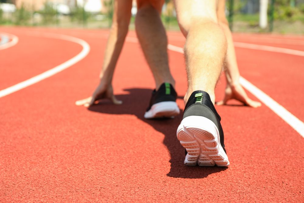 Sportsman low starting to run on red athletic track, close up