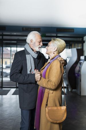 Cute mature couple in winter coat and scarf embracing inside hotel