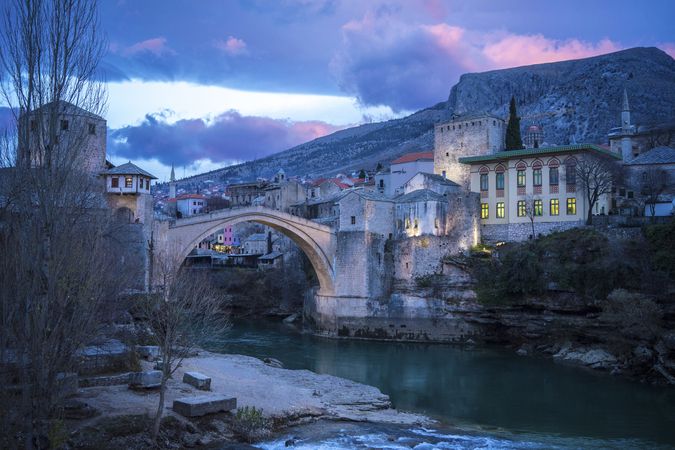Amazing landscape of medieval bridge and aged buildings under vibrant dramatic clouds during sunset