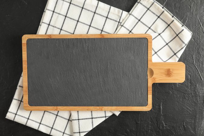 Cutting board with kitchen towel on dark background, top view