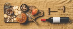 Cheese plate with bottle of red wine, cork screws on light brown linen, wide composition