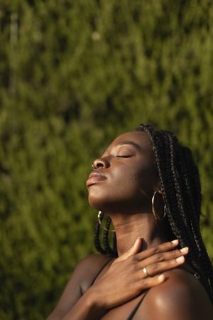 Close-up portrait of a young Black woman resting her hand over her shoulder with her eyes closed