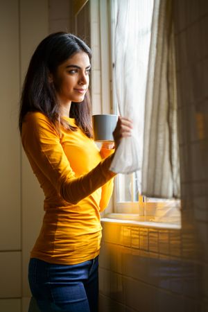 Vertical composition of woman enjoying view out the window with warm beverage