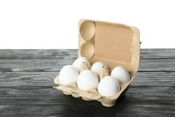 chicken eggs in carton box on wooden table isolated on light background, space for text