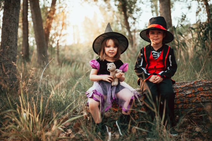 Brother and sister sitting on log dressed as skeleton and witch