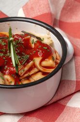 Bowl of delicious ravioli with tomato sauce and rosemary on table cloth