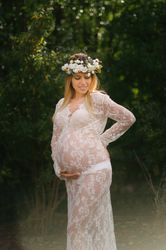 Pregnant woman with closed eyes in white lace dress touching chin while standing in forest