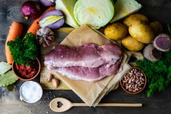 Ingredients for hearty stew with meat surrounding cutting board