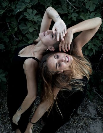 Young women posing near green bush