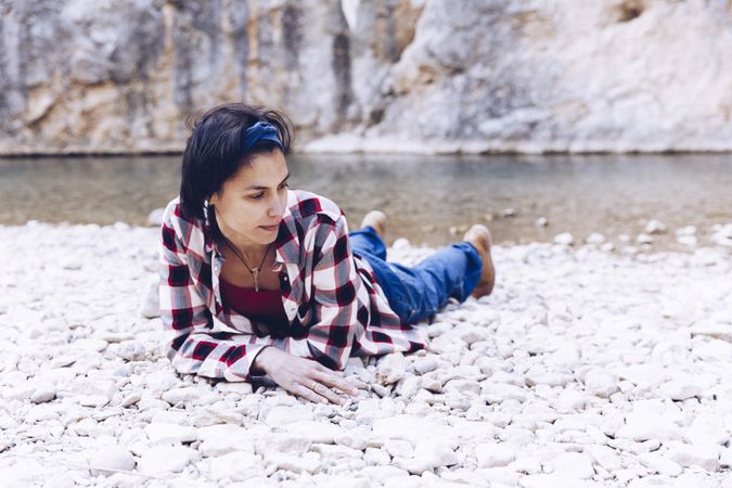 Positive woman resting on stone shore near river