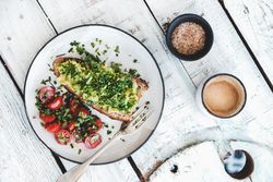 Avocado toast on sourdough bread, cherry tomatoes, coffee and bowl, on light background, top view