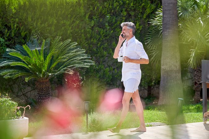 Adult man with cup of coffee talking on smartphone on terrace