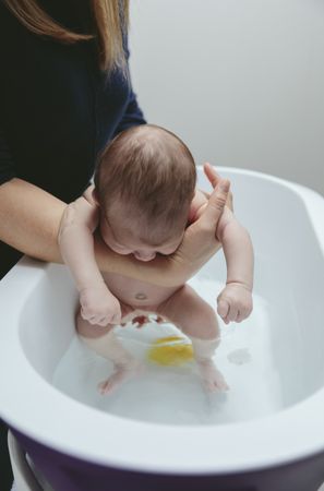 Newborn in the bathtub held by her mother