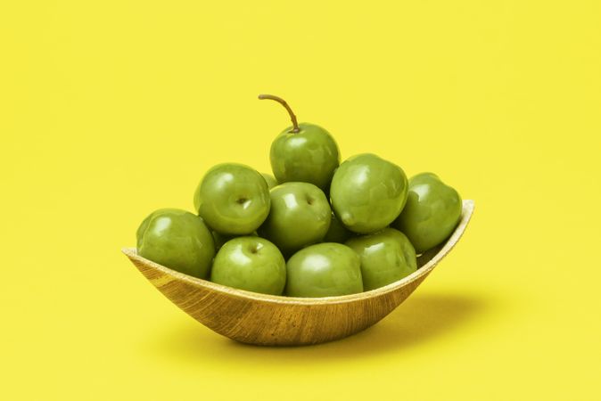 Green olives in eco friendly wooden bowl isolated on yellow background
