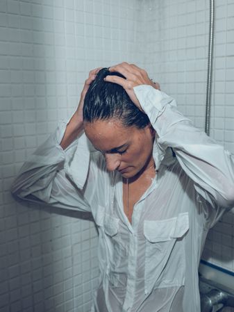 Exhausted woman in wet shirt touching head under shower
