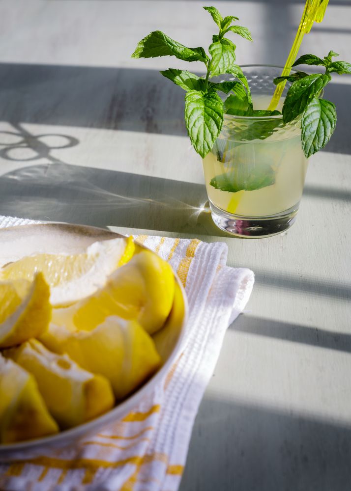 Glass of fresh lemonade next to plate with cut lemons on table