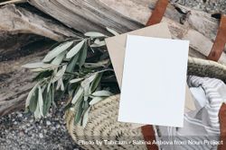 Blank greeting card invitation mockup in straw bag with olive tree branches and towel 5ngRLn