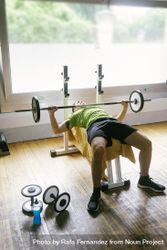 Man in green t-shirt lifting heavy bar on bench working out arms and chest 5kBYj0