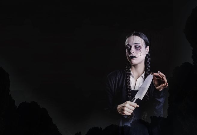 A woman with long braids, with gothic and dark look, plays with a butcher knife