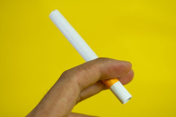 Side view of hand holding cigarette on yellow background