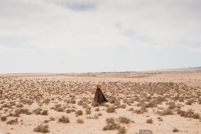 Woman in long robes walking through dry landscape with basket on head