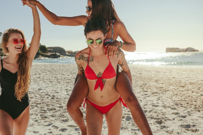 Woman piggy back riding on her friend and holding hand of female beside her