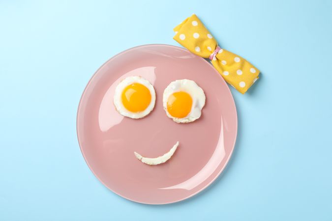 Looking down at pink plate with smiley face on it made of eggs and condiments