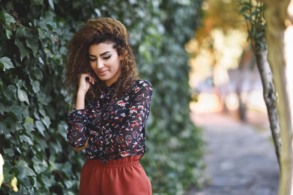 Arab woman wearing casual clothes in the street lined with greenery looking down