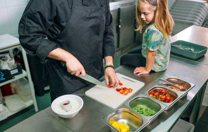 Unrecognizable chef teaching little girl how to prepare healthy poke bowl in a professional kitchen
