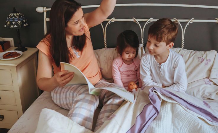 Portrait of woman playfully reading book to her daughter and son in bed