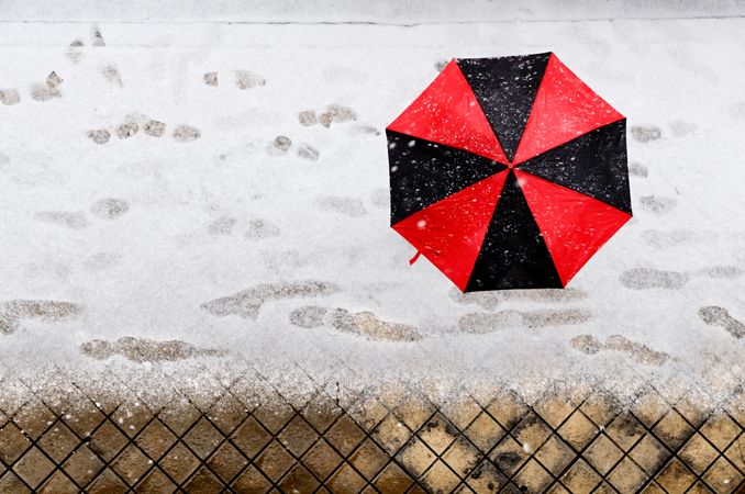 Top of red and dark umbrella shielding person from snowfall
