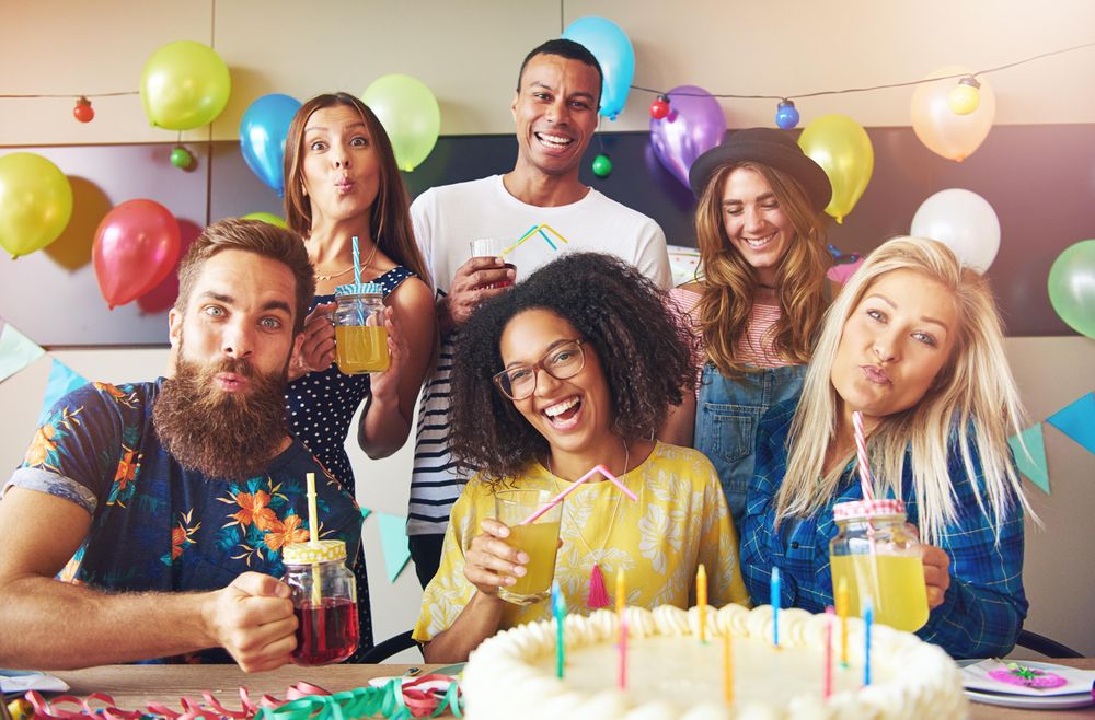 Friends smiling with drinks, balloons and birthday cake with candles