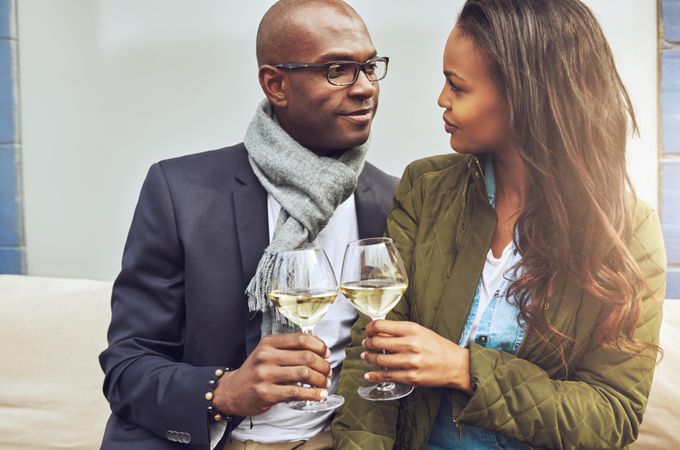 Black couple looking into each others eyes and toasting with glasses of wine