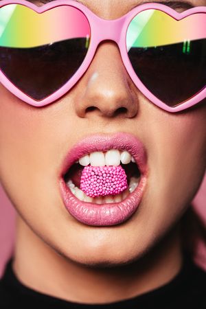 Close up of woman in heart shape pink sunglasses biting candy