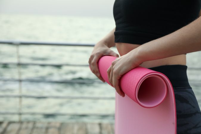 Yoga mat in female hands on sea, space for text