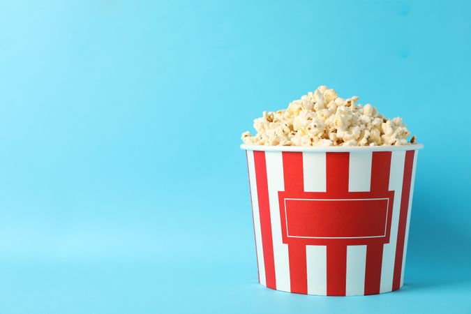 Striped bucket with popcorn on blue background, space for text