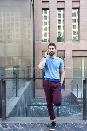 Young bearded man leaning on railings while talking on mobile phone