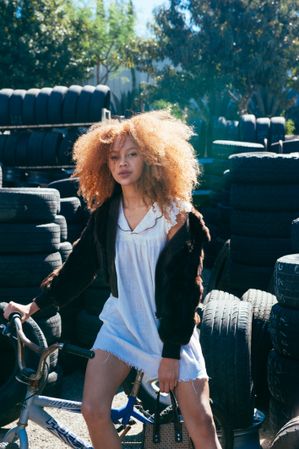 Portrait of young woman with afro looking at camera at tire shop with sun behind