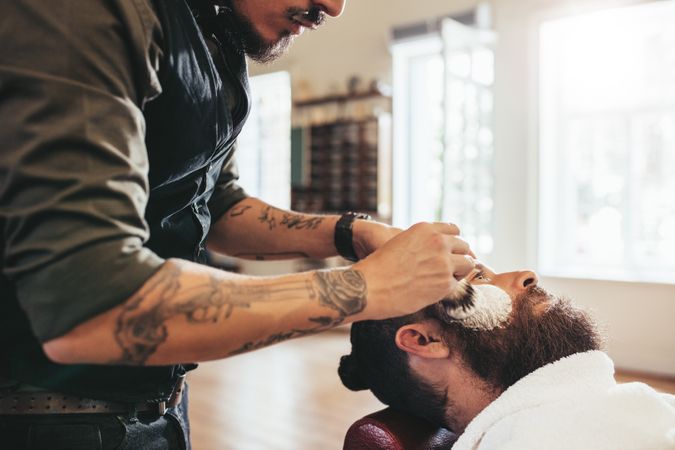 Barber applying shaving cream to male customer
