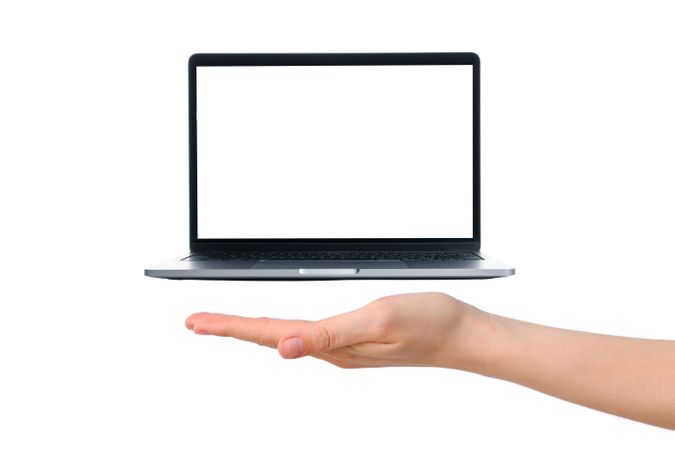 A hand supports a modern laptop hovering above a clear surface